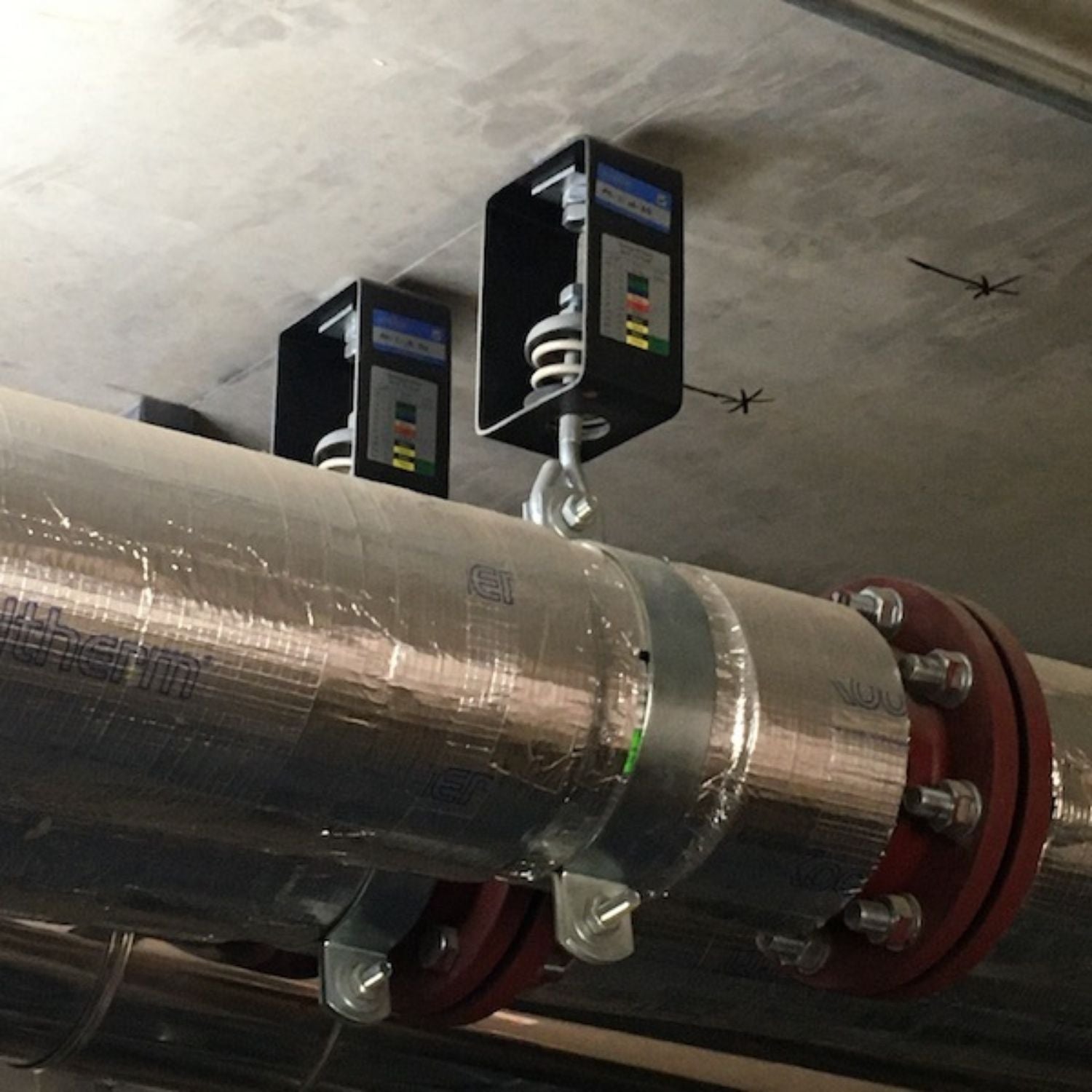 Detailed close-up of Acrefine housed spring hangers mounted on a rod suspension system holding an insulated pipeline.
