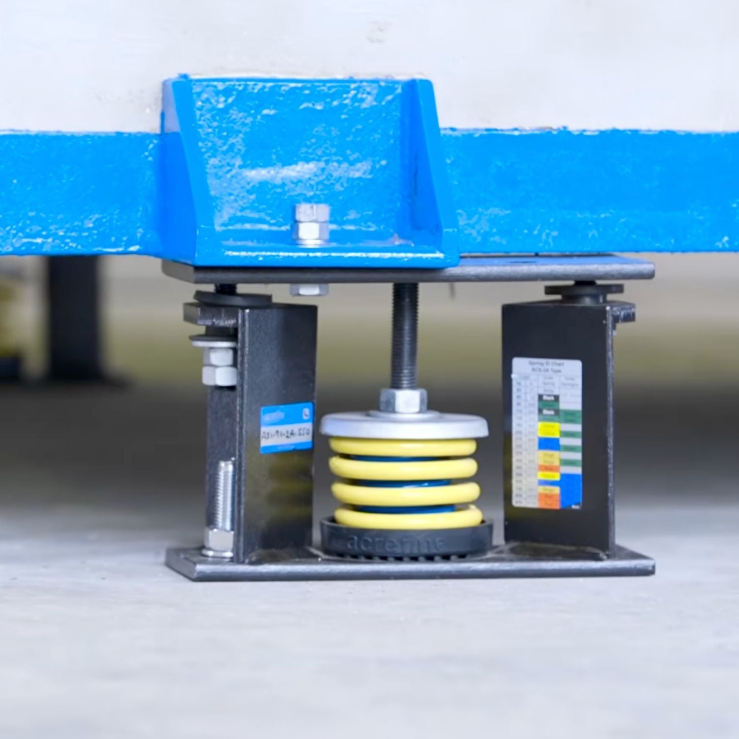 Acrefine seismic spring isolator with yellow coil bolted under a blue industrial inertia base.