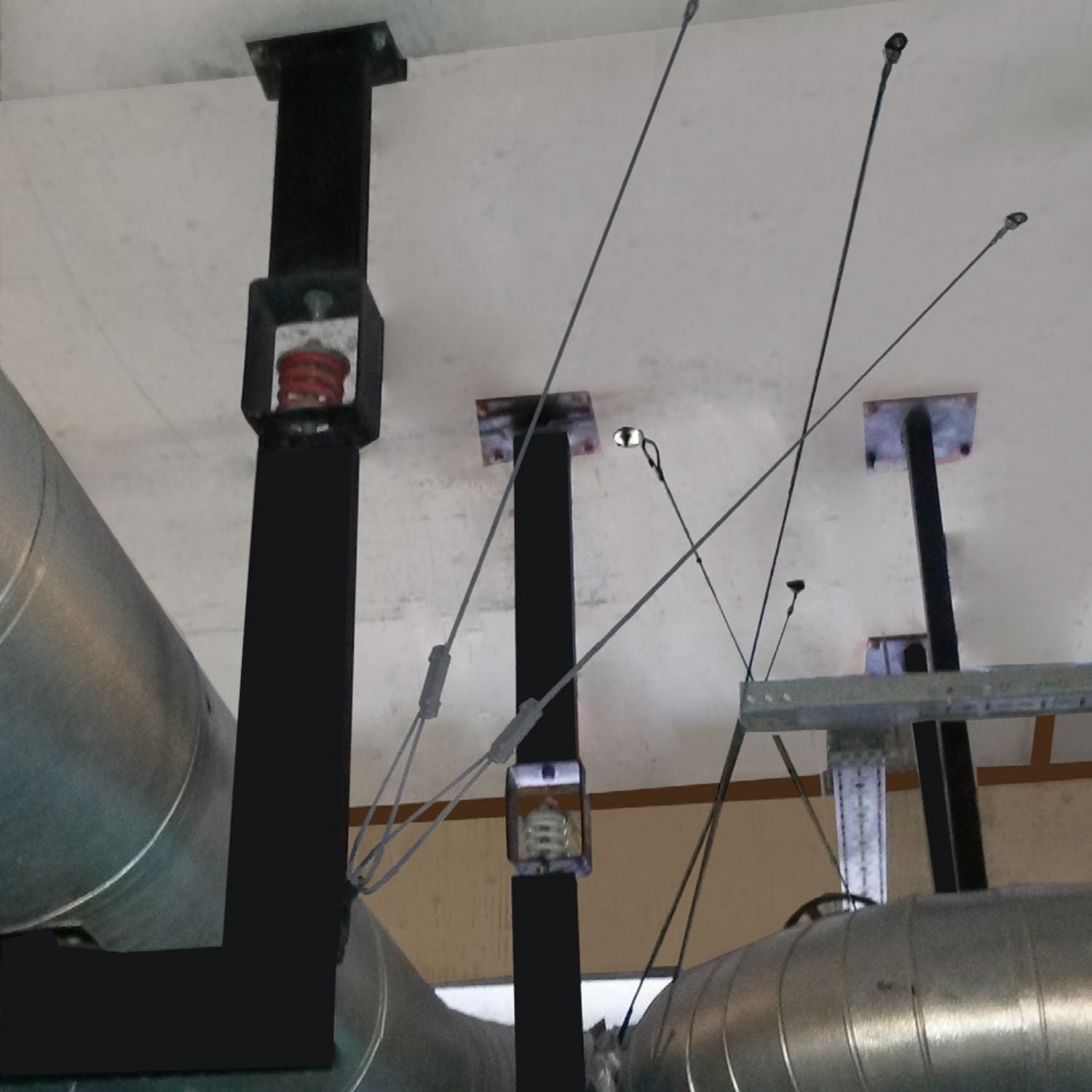 Acrefine spring hanger isolators installed on ceiling brackets for industrial pipe suspension and vibration control.
