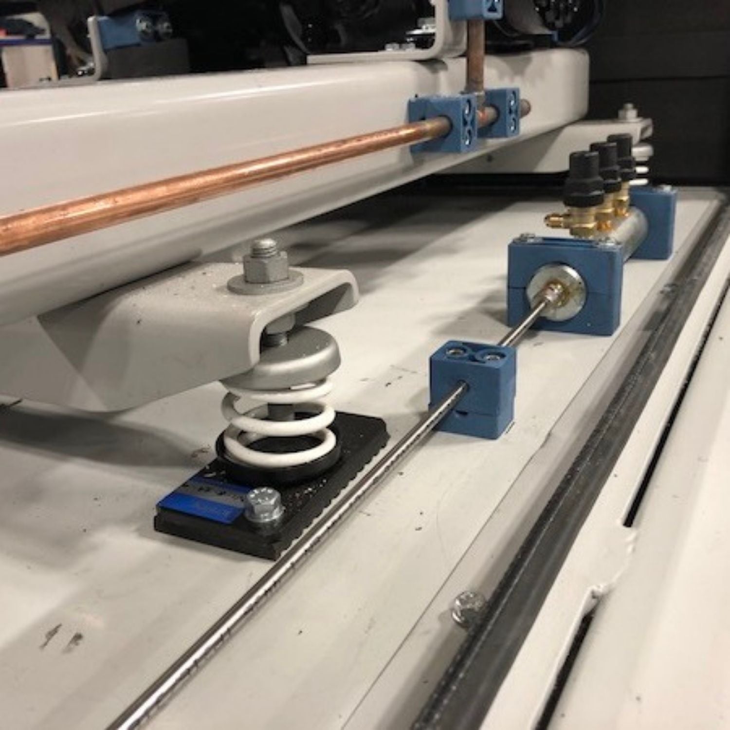 Acrefine white spring isolator with a bolted bottom plate installed under mechanical equipment for vibration control.