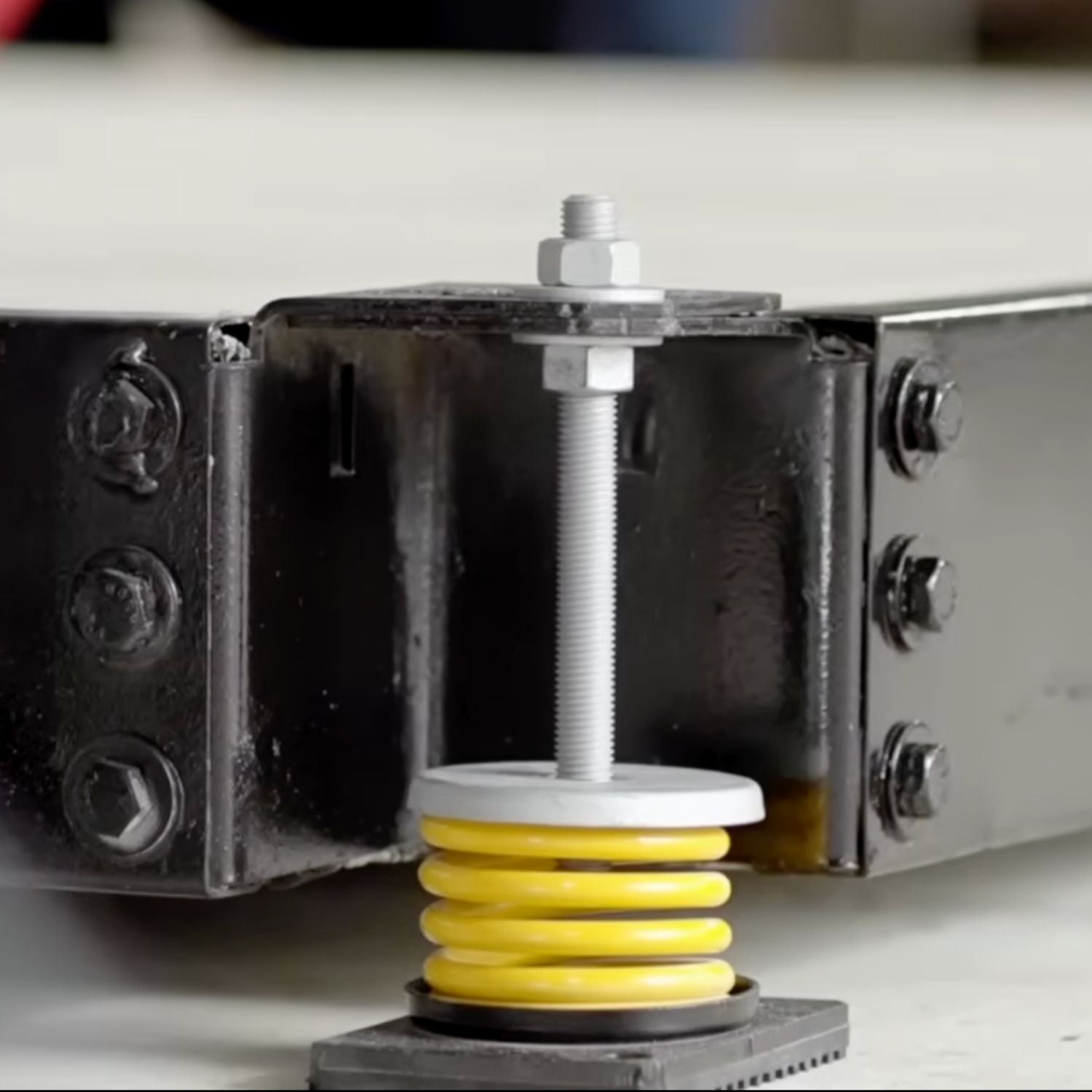 Detailed view of Acrefine yellow spring isolator with base plate positioned beneath a heavy industrial inertia base.