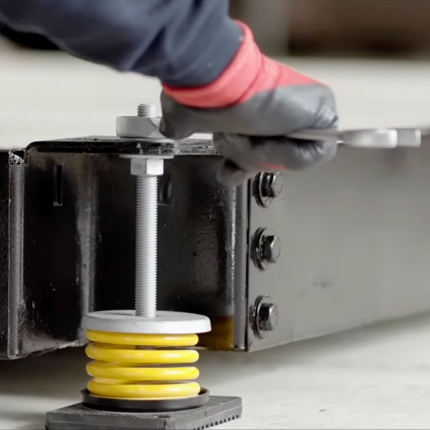 Technician adjusting the top leveling nut of an Acrefine yellow spring isolator with base plate during equipment installation.