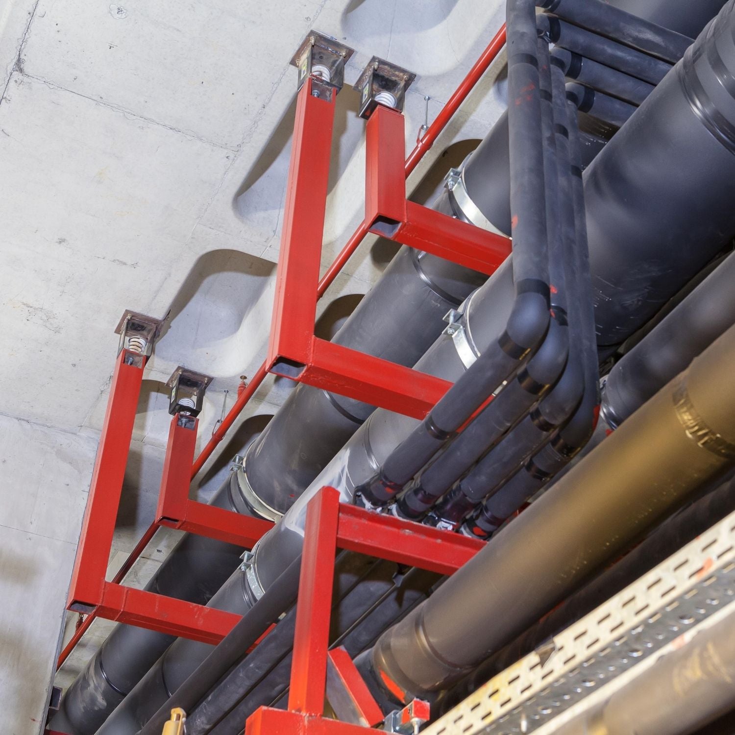 Acrefine vibration hanger isolators suspended from concrete ceiling supporting large industrial insulated piping layout.