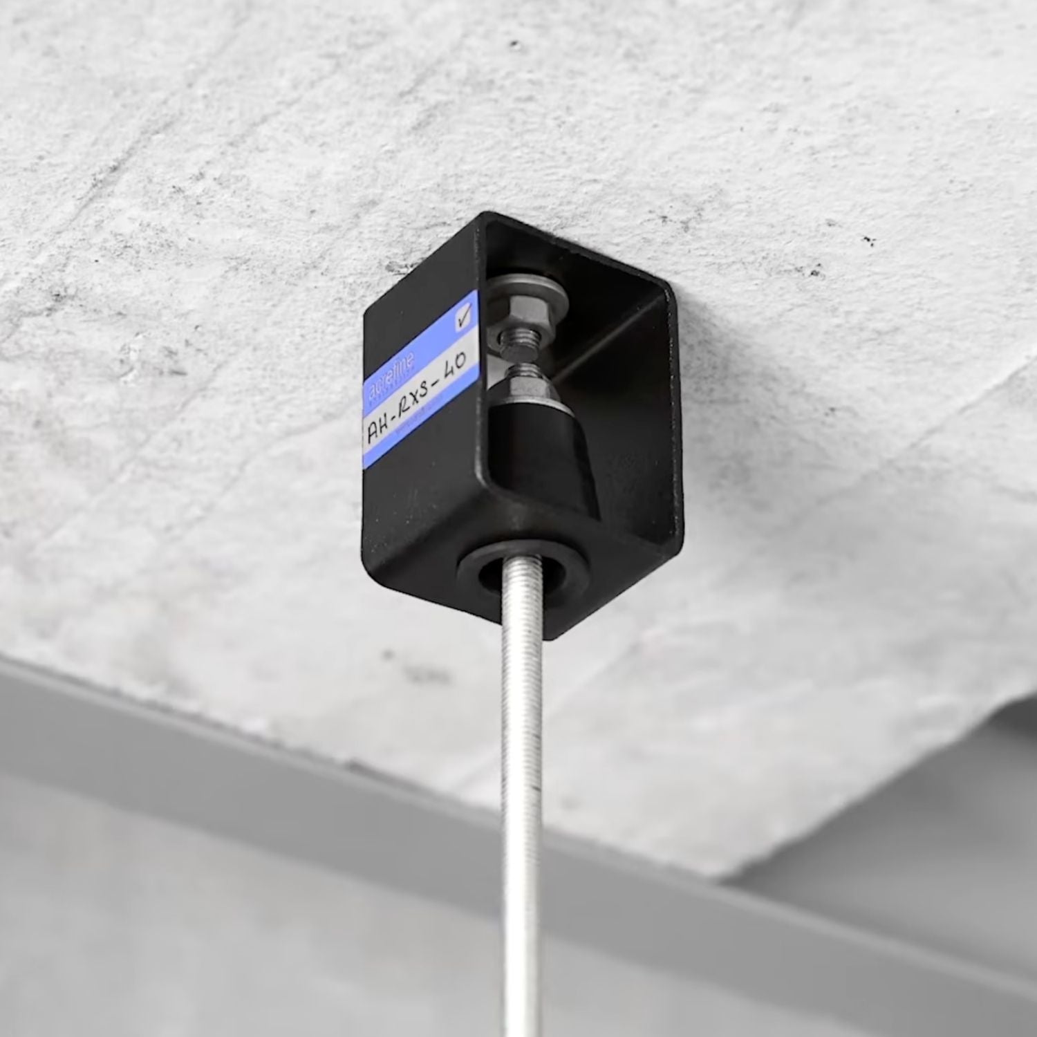 Acrefine rubber hanger isolator enclosed in steel housing, mounted to a concrete ceiling with a threaded suspension rod.