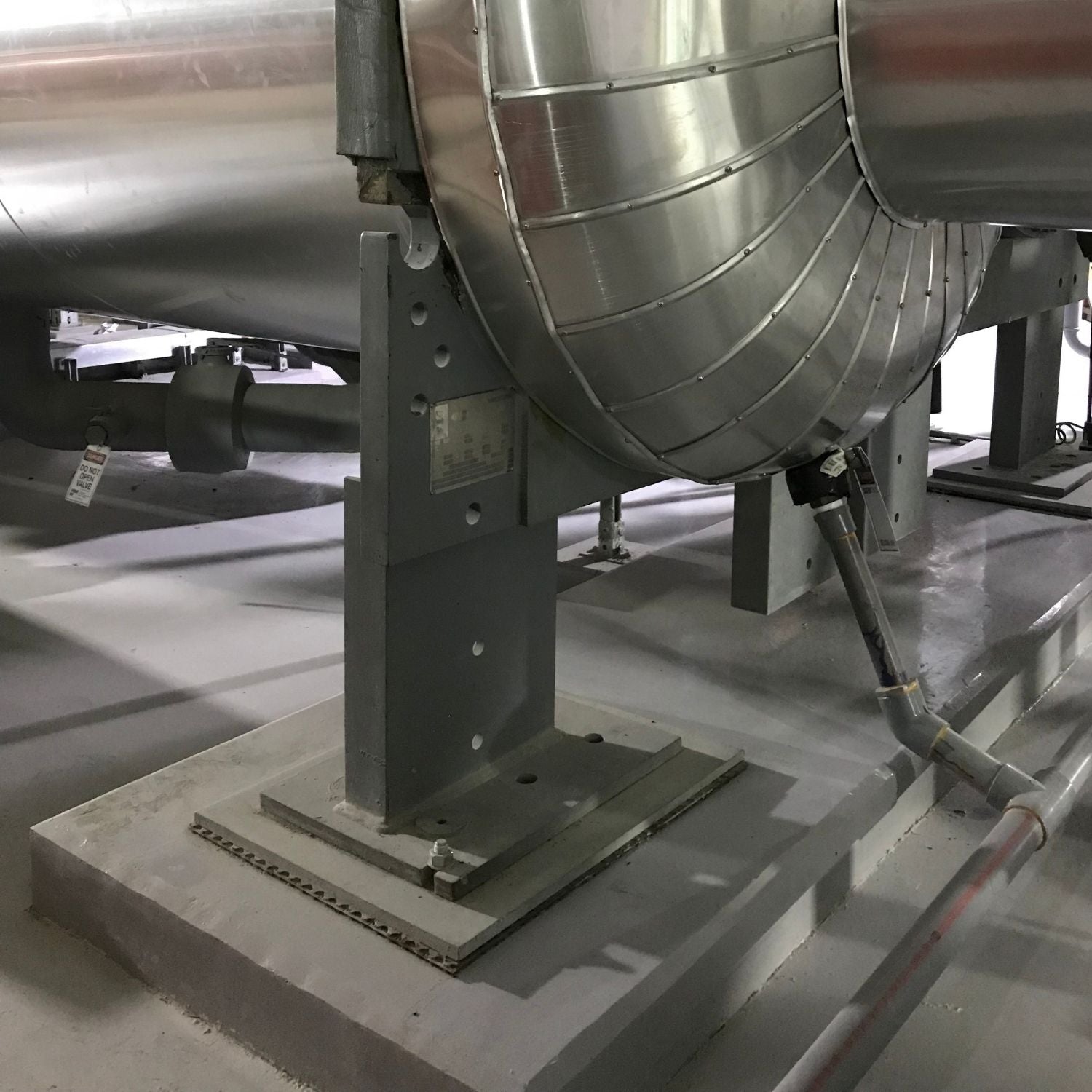 Acrefine solid rubber isolation pad installed beneath a heavy industrial pipeline support framework on a concrete plinth.