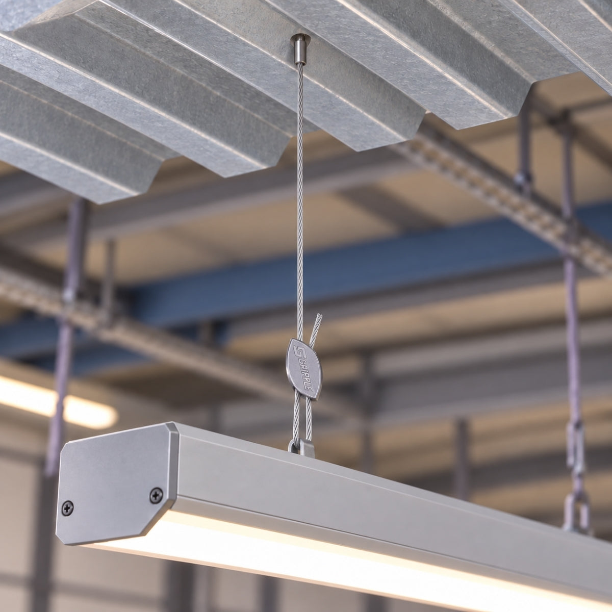 Linear light fittings suspended from cladding hooks under a profiled metal roof.