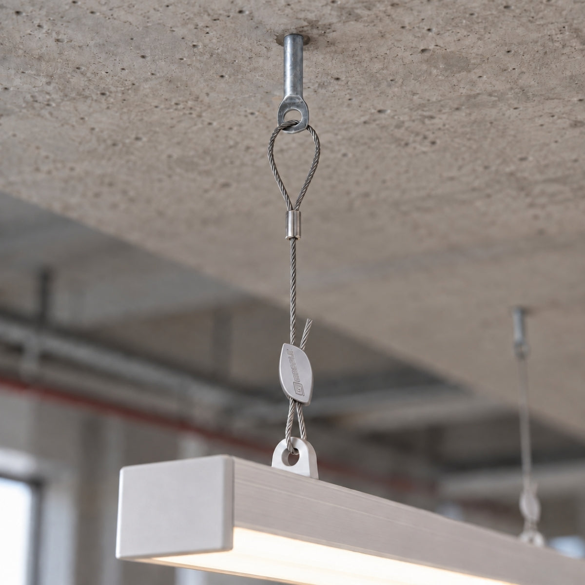 A ceiling anchor fixed into a concrete soffit, carrying a wire hanger and a linear LED fitting.