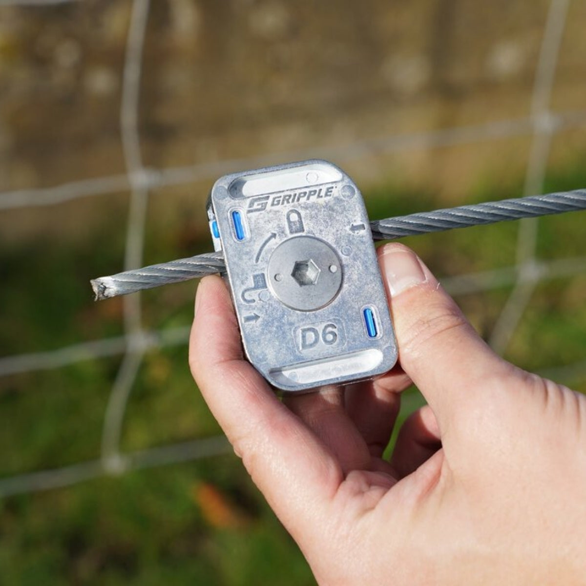 A hand holding a Gripple Dynamic on a wire fence line outdoors.