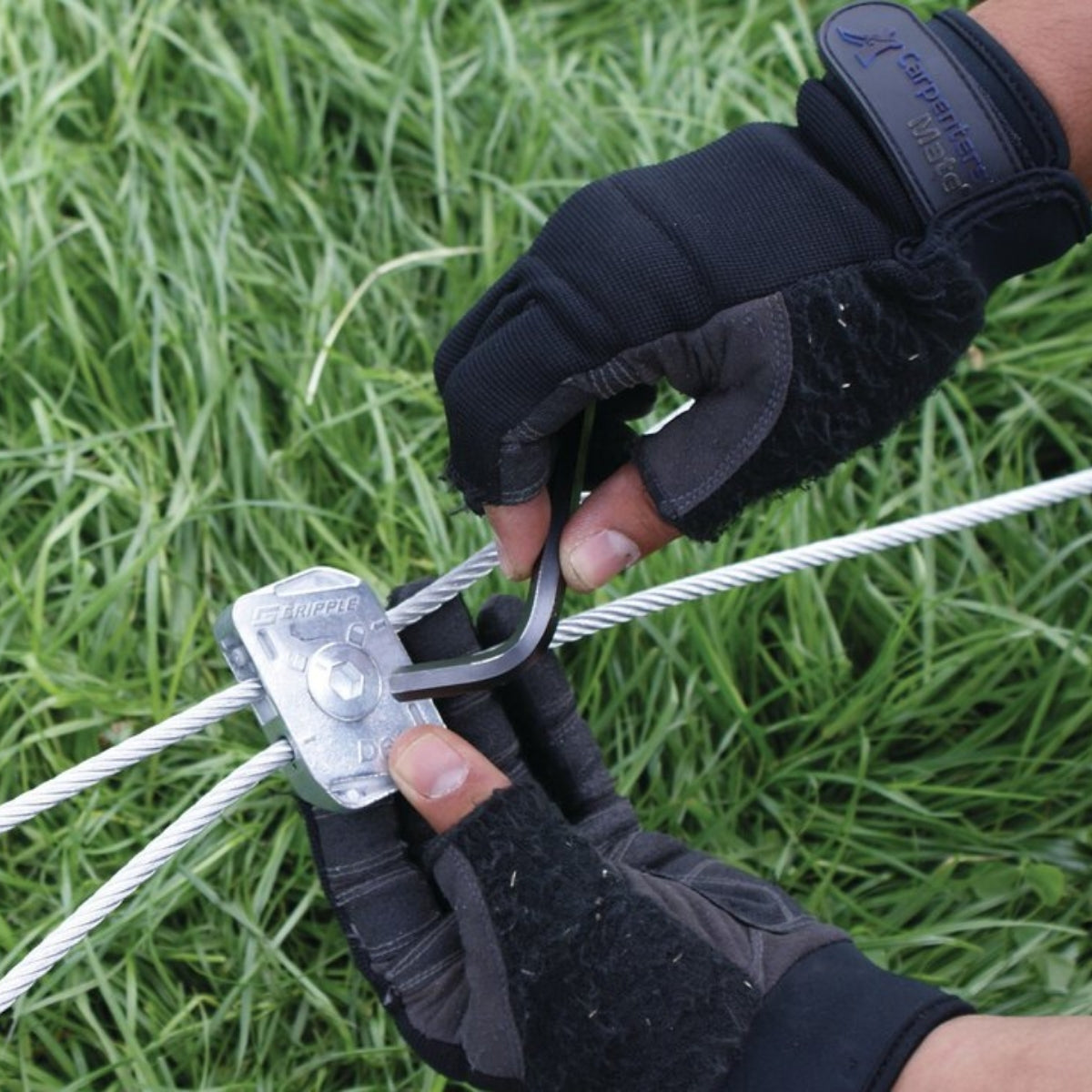 Gloved hands fitting a Gripple Dynamic to a fence wire over grass.