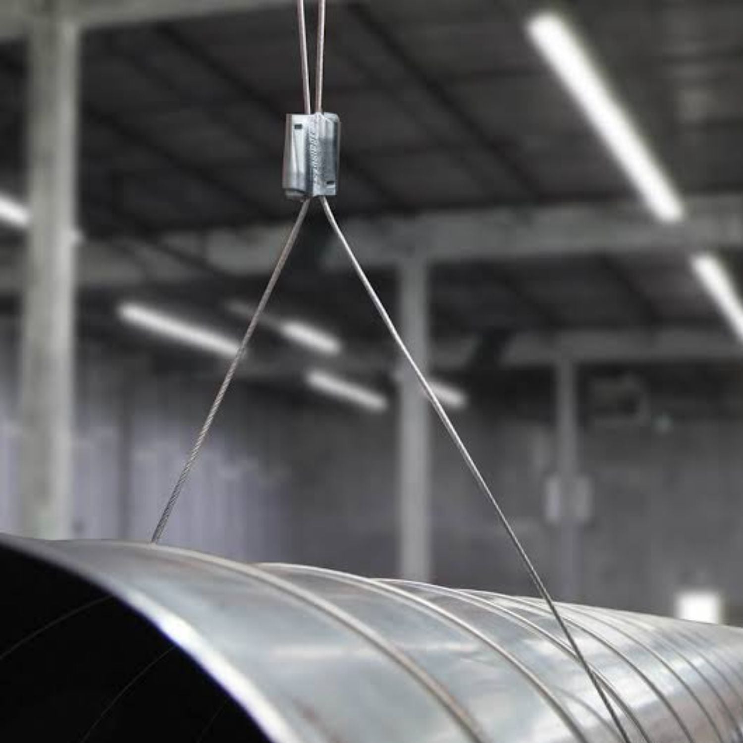 A Gripple Express fastener mechanism suspended in mid-air holding a circular metal HVAC ventilation duct using a looped wire cable.
