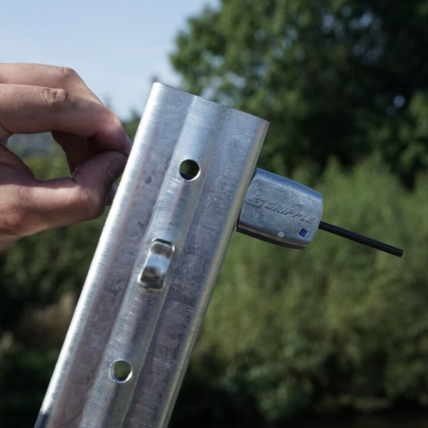 An installer inserting a trellis line into a Gripple GP unit through a punched hole in a metal end post profile during installation.