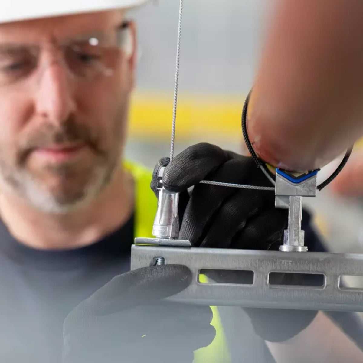 A worker in safety glasses fitting the QT clamp bracket overhead.
