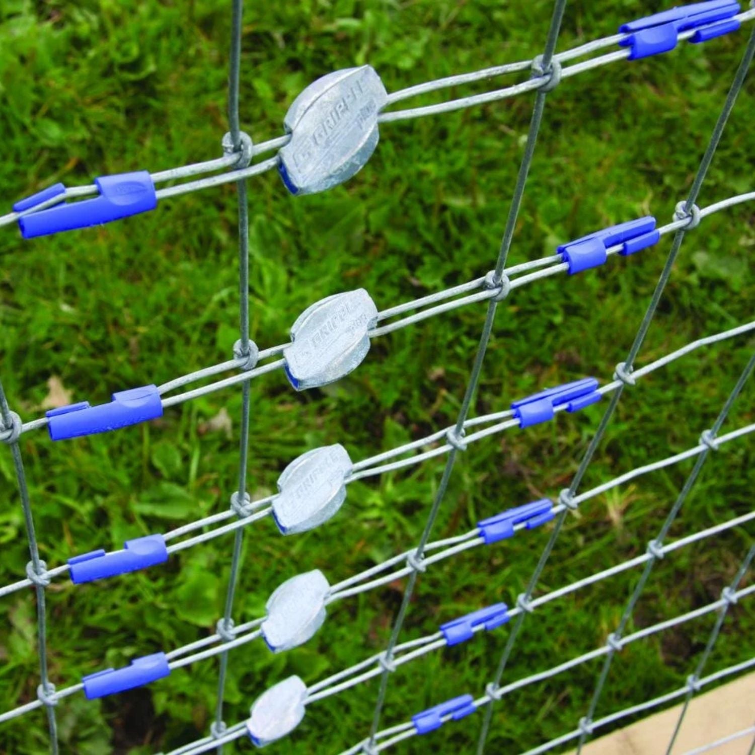 Multiple silver Gripple Plus wire tensioners with blue twisters installed horizontally across a wire mesh field fence.