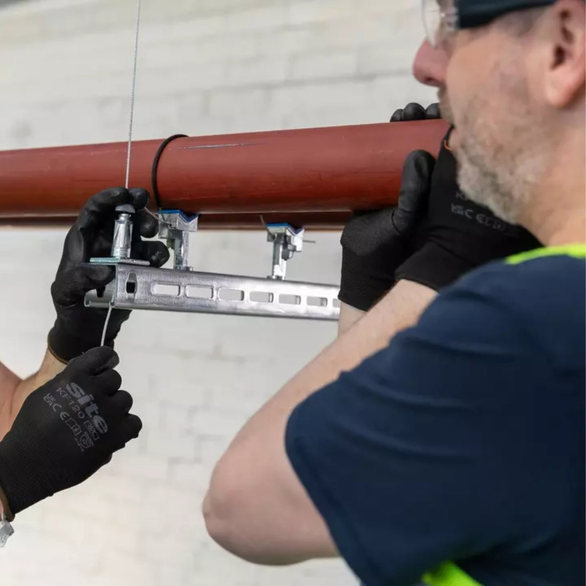 A worker securing an orange pipe into a QT clamp bracket.