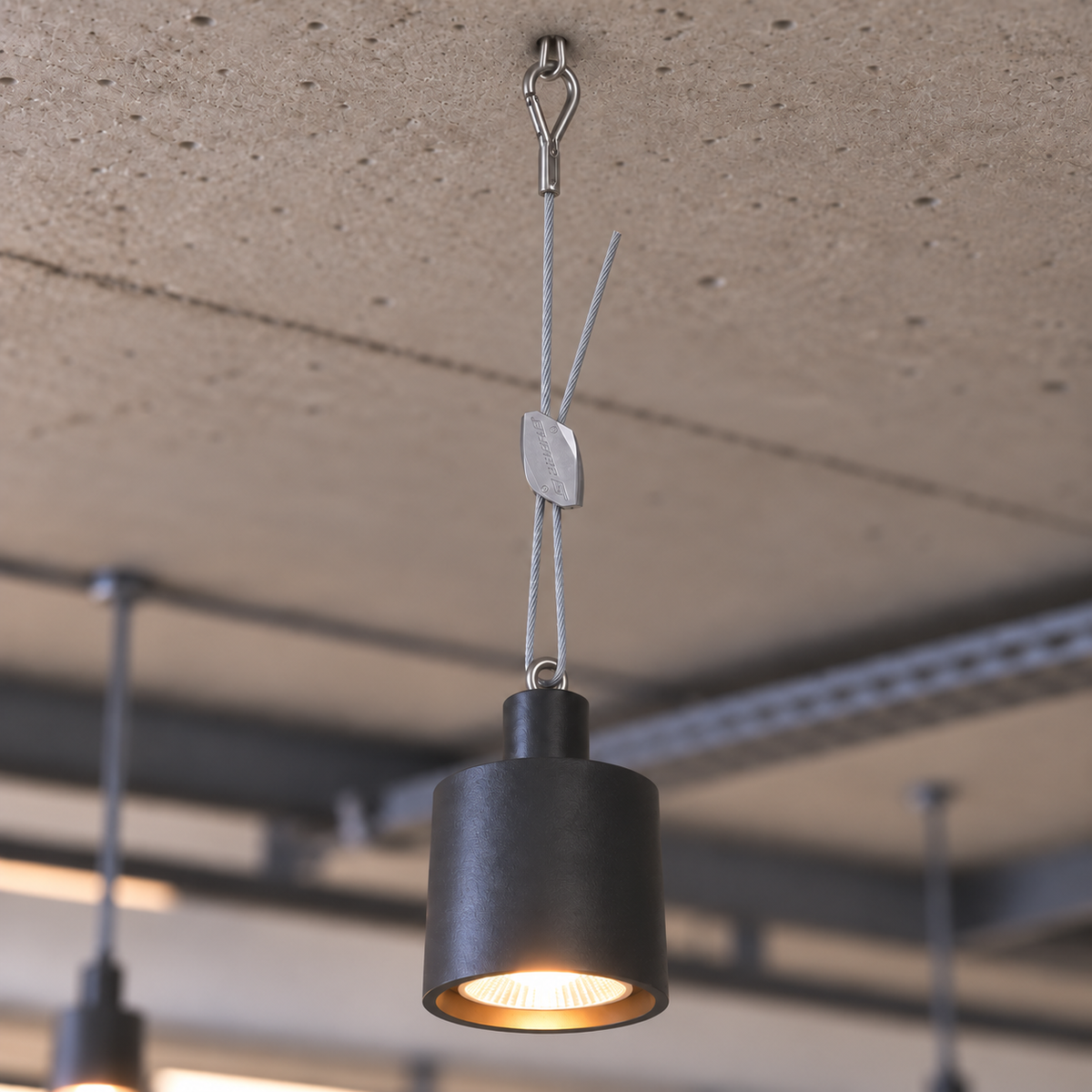 A pendant spotlight suspended from a snap hook hanger under a concrete ceiling.