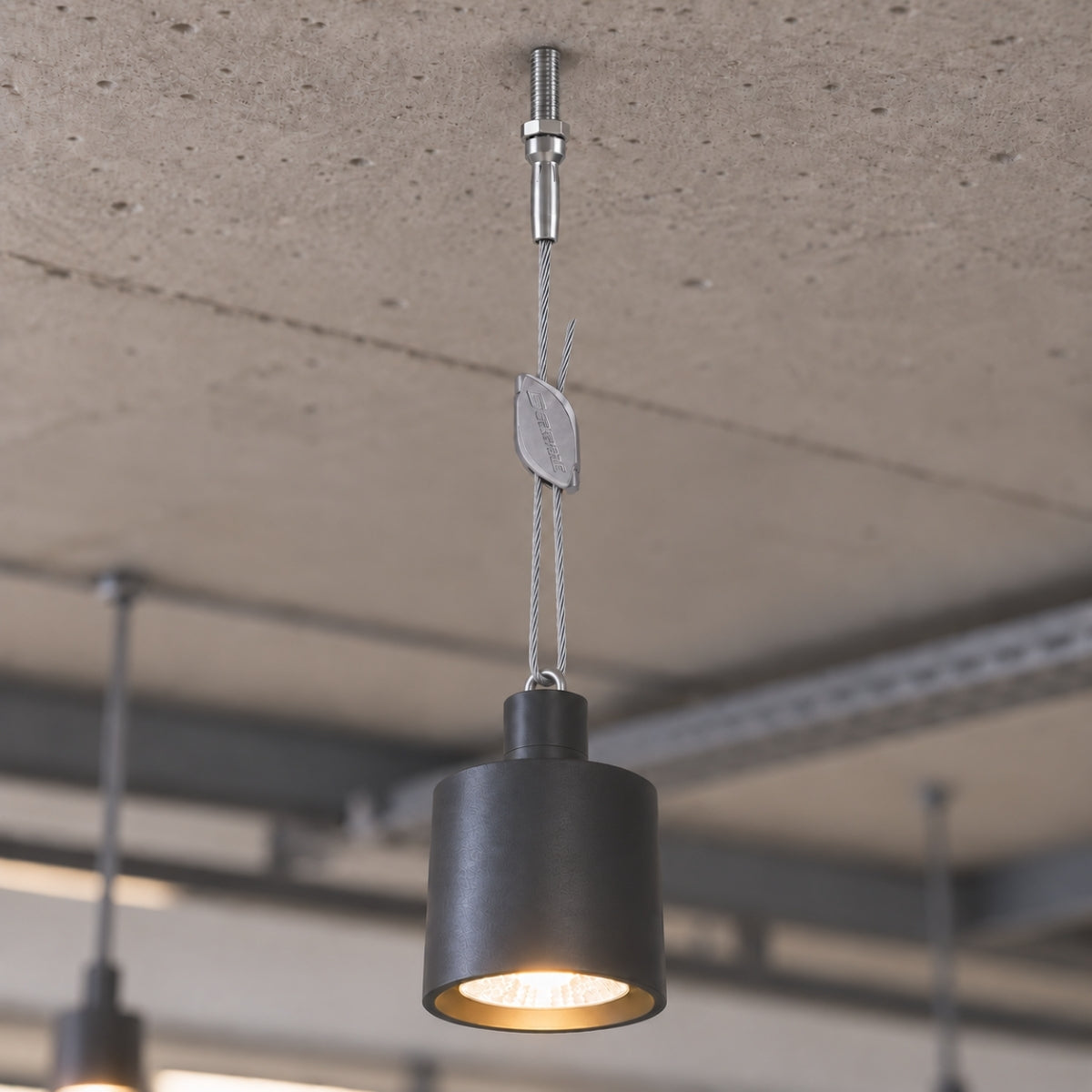 A pendant spotlight suspended from a stud hanger below a concrete ceiling.
