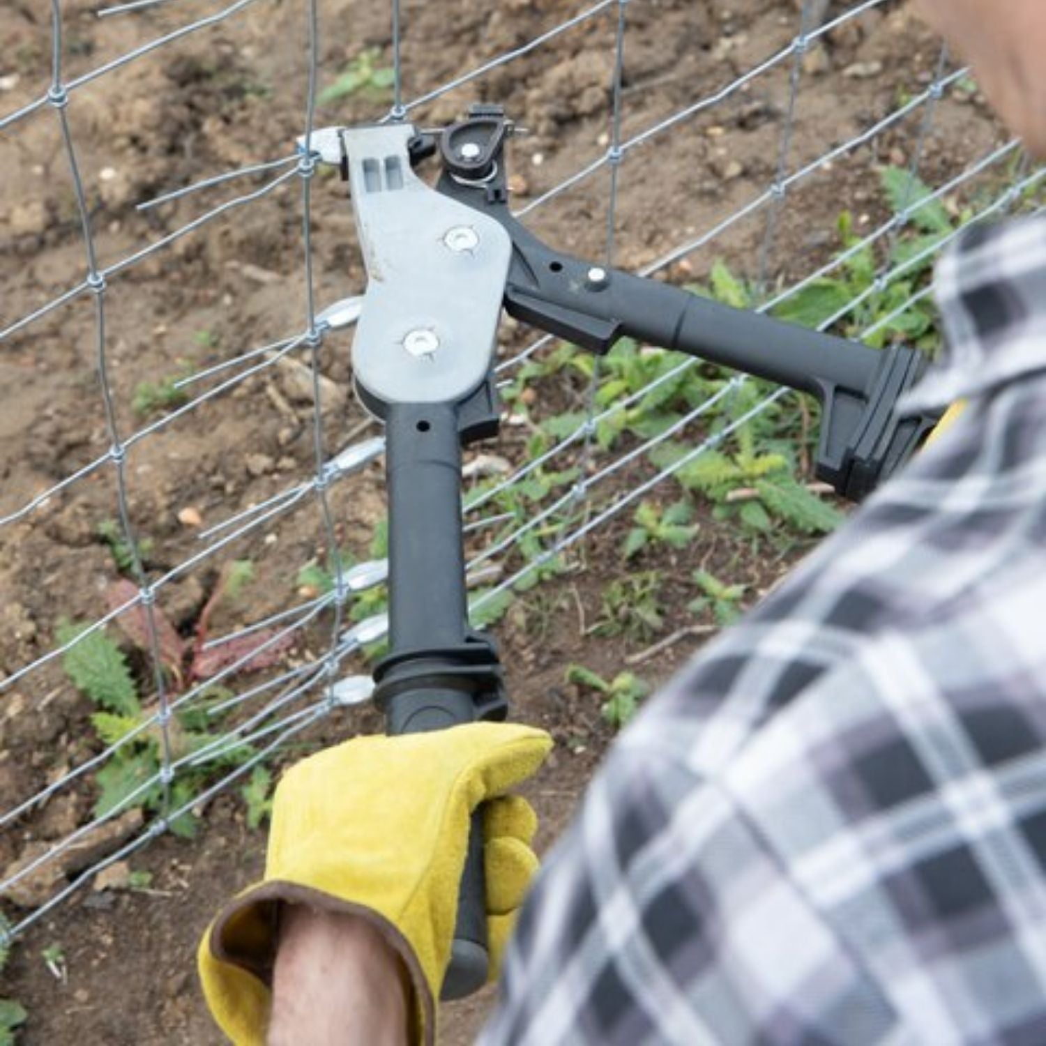 An installer using the Gripple tensioning tool to tighten a wire mesh fence installation outdoors.
