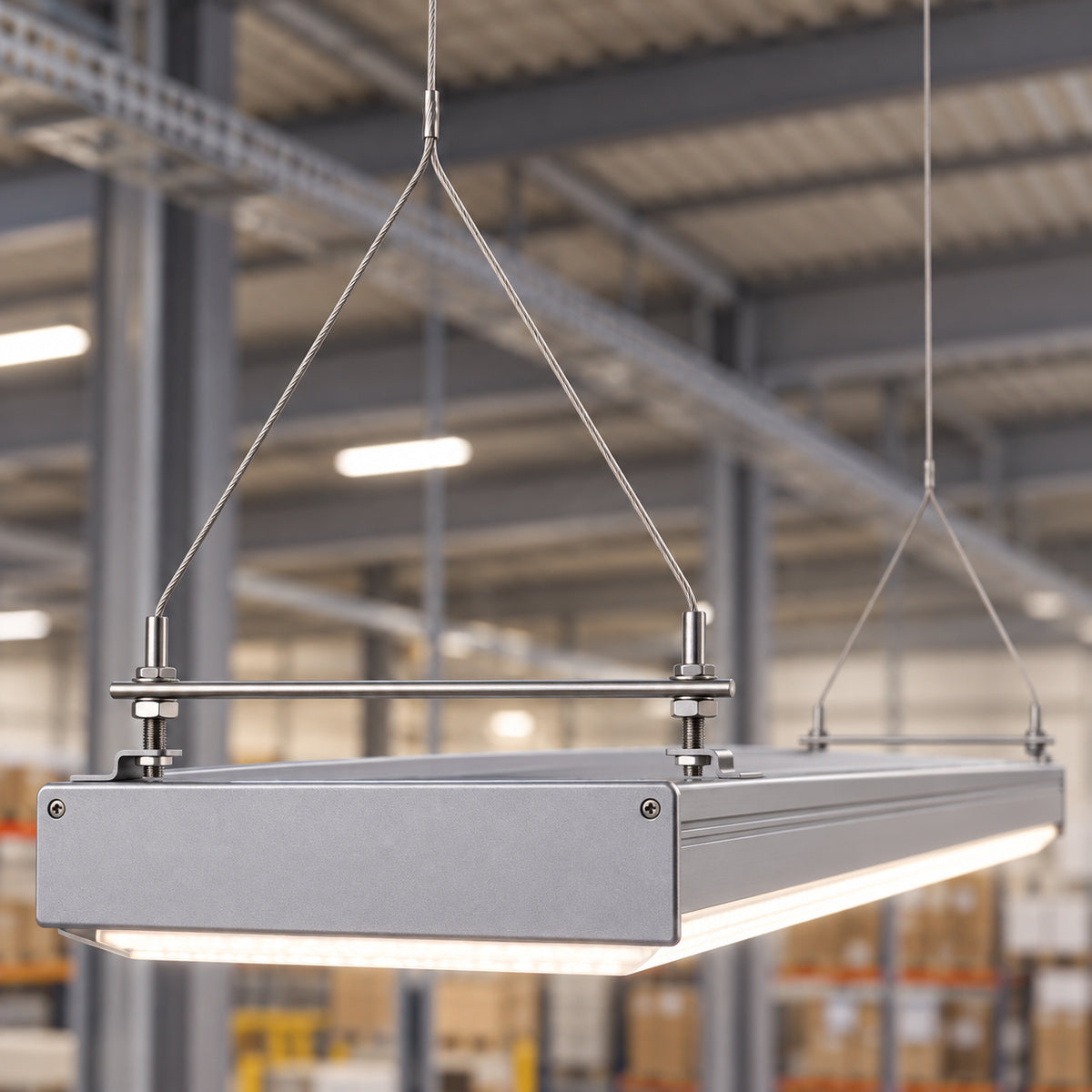 A linear LED fitting suspended on wire hangers from a warehouse ceiling.
